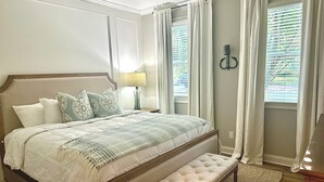 A neatly arranged bedroom with a large bed, a bench, a nightstand, and a lamp.