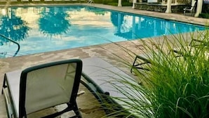 A swimming pool with lounge chairs and a pergola, surrounded by greenery.