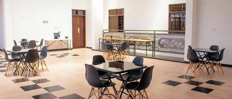 Un espace intérieur spacieux, doté de plusieurs tables et chaises, d’un sol à motifs et d’un balcon avec une balustrade.