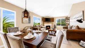 A spacious living room with a fireplace, a dining area with a wooden table set for a meal, and a cozy seating area with a sofa and armchairs. - Mins To Beach, Perfect For Families, Amazing Views (Newport Beach)