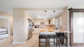 A modern kitchen with a central island, bar stools, and a large window. - Mins To Beach, Perfect For Families, Amazing Views (Newport Beach)