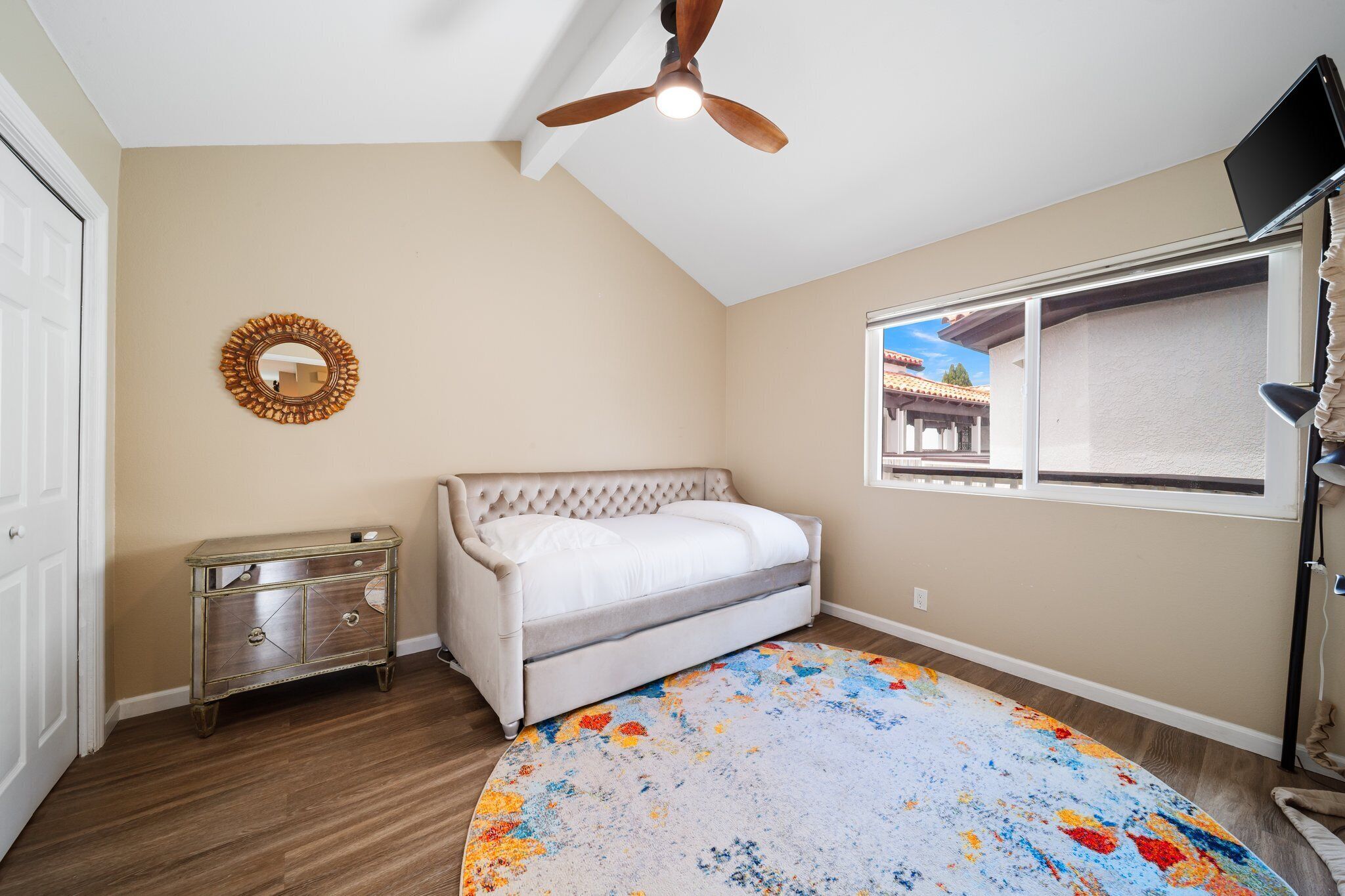 A bedroom with a bed, a ceiling fan, a window, a dresser, and a rug.