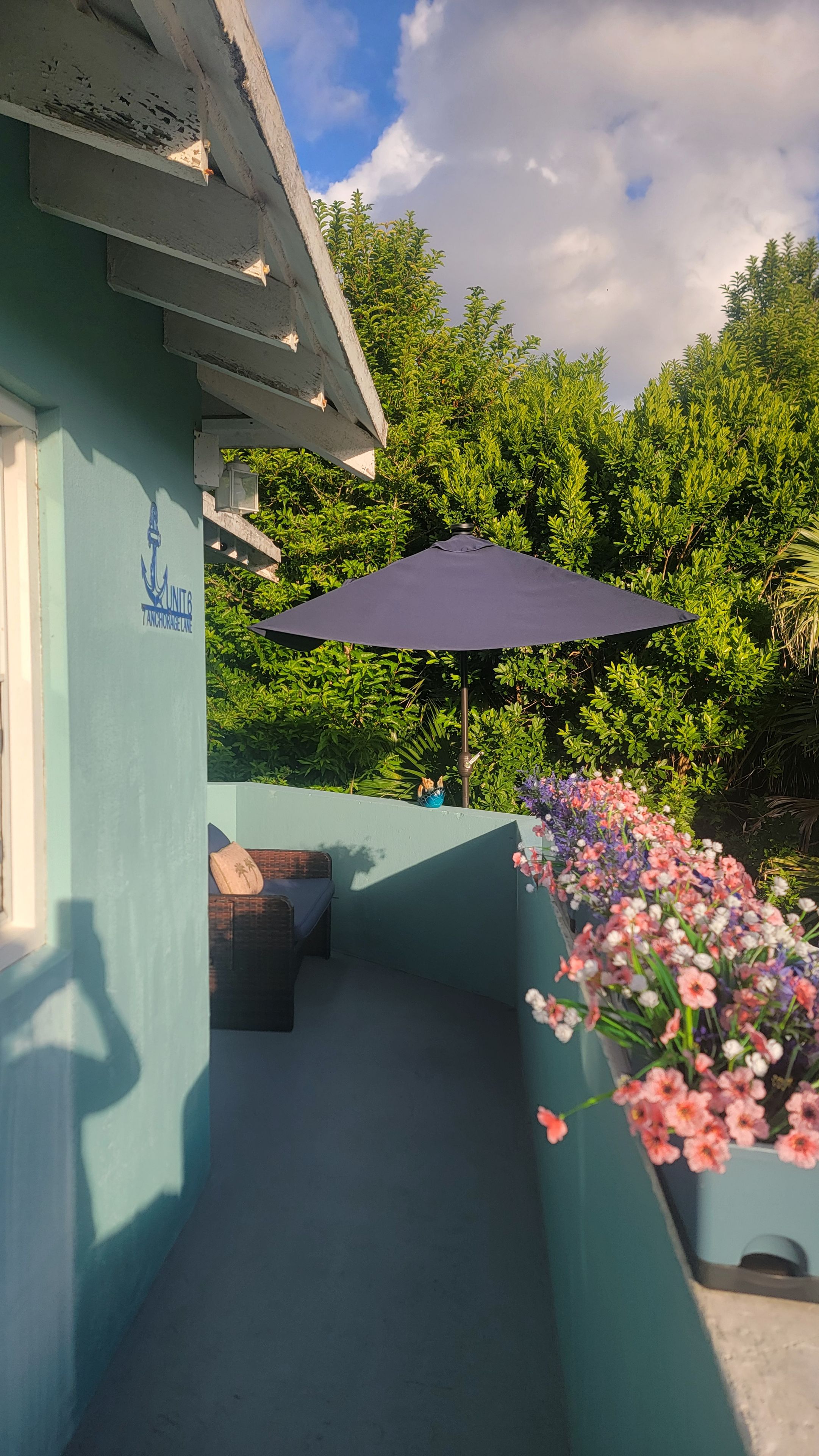 Un balcón con un toldo azul, una jardinera con flores y un letrero con un logotipo.