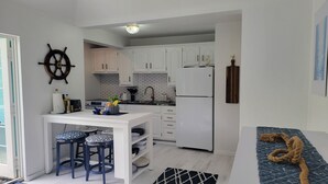 Cocina compacta con armarios blancos, una isla central con taburetes, un refrigerador y un timón decorativo.