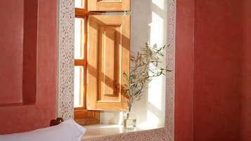 A room with a window, wooden shutters, and a vase with a plant.