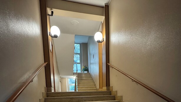 A staircase with a handrail, leading to an interior space with a ceiling light and a window.