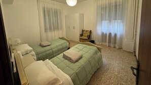 A room with two single beds, a chair, a wardrobe, and a ceiling light.