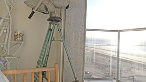 A balcony with a telescope, a wooden chair, and a view of the beach. - Apartment in Het Zoute Near Place Rubens (Knokke-Heist)