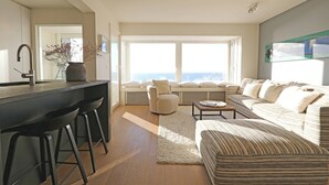A modern living room with a sofa, a coffee table, and a bar area with stools. - Apartment in Het Zoute Near Place Rubens (Knokke-Heist)