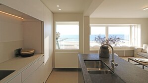 A modern kitchen with a large window overlooking the sea, a built-in oven, and a sink with a faucet. - Apartment in Het Zoute Near Place Rubens (Knokke-Heist)