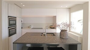 A modern kitchen with built-in appliances, a granite countertop, and a window with a view. - Apartment in Het Zoute Near Place Rubens (Knokke-Heist)