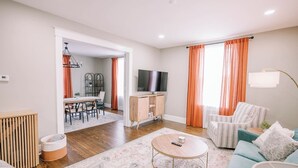 A modern living room with a sofa, coffee table, TV, and a dining area with chairs and a table. - Victorian Modern 3bd/2bath - Meredith’s Place (Danville)