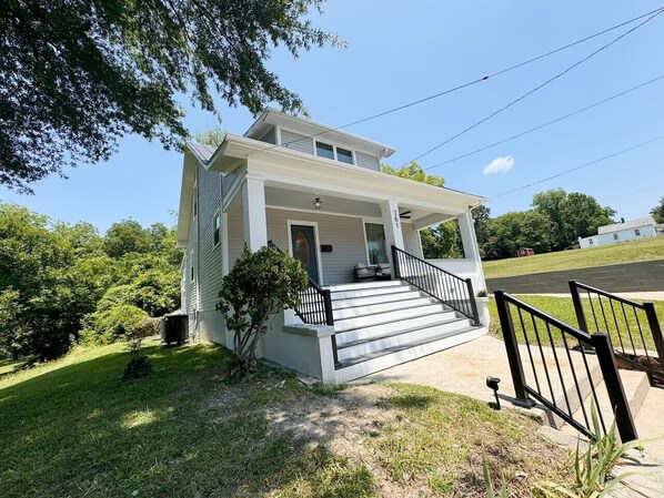 A two-story house with a front porch, a small front yard, and a black metal fence.