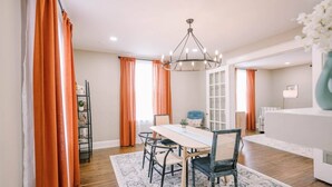 A dining area with a table, chairs, a chandelier, and orange curtains. - Victorian Modern 3bd/2bath - Meredith’s Place (Danville)