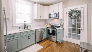 A modern kitchen with white cabinets, a stainless steel dishwasher, a microwave, and an oven. - Victorian Modern 3bd/2bath - Meredith’s Place (Danville)