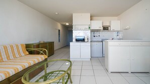 A compact living space with a sofa, a dining table, a kitchen area with a refrigerator, microwave, and cabinets. - Apartment in Agde With Direct Beach Access (Agde)