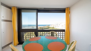 A balcony with a table and chairs, a view of the sea, and yellow curtains. - Apartment in Agde With Direct Beach Access (Agde)