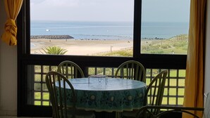 A dining area with a table and chairs, a view of the beach, and a large window with curtains. - Apartment in Agde With Direct Beach Access (Agde)
