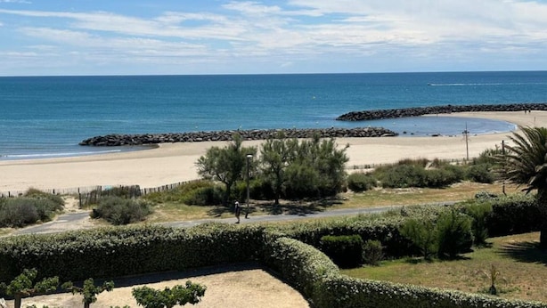 A beach with a rocky breakwater, a sandy shore, and a clear blue sky. - Apartment in Agde With Direct Beach Access (Agde)