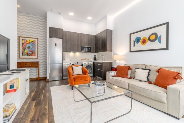 A modern living room with a sofa, coffee table, and a kitchen area with appliances.