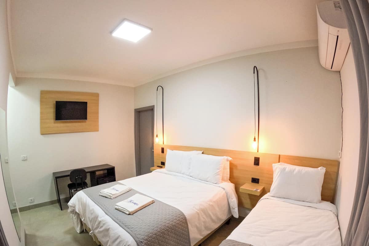 Une chambre d’hôtel avec deux lits, un téléviseur à écran plat fixé au mur et un bureau avec une chaise.