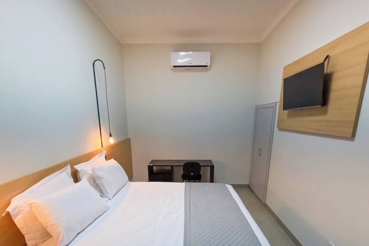 Une chambre d’hôtel équipée d’un lit, d’un bureau, d’un téléviseur fixé au mur et d’un appareil de climatisation.