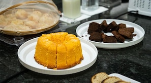 A table with a yellow dessert, a plate of brownies, and a basket of round pastries. - Terraço Plaza Hotel (Jaboticabal)