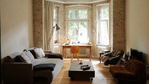Un salon confortable avec un canapé, un fauteuil et une table basse, un bureau avec une lampe et un téléviseur.