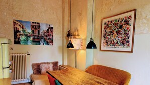 Une pièce chaleureuse avec une table à manger en bois, une chaise rouge et turquoise, un radiateur et deux lampes fixées au mur.