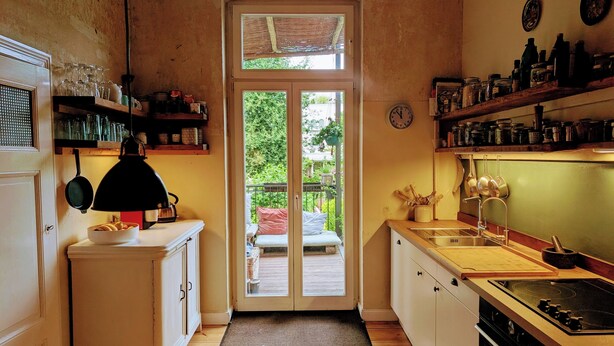 Une cuisine avec un plancher en bois, une cuisinière, un évier et une fenêtre donnant sur un balcon.