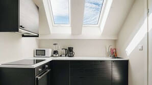 A modern kitchen with a built-in oven, microwave, and coffee maker, featuring dark cabinetry and a skylight.