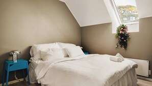 A bedroom with a bed, a nightstand, a radiator, and a window with a view of buildings.
