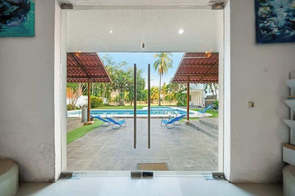 A view of a swimming pool area with two lounge chairs and a covered seating area.