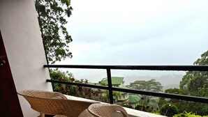 Un balcon avec des fauteuils en osier et une vue sur un immeuble dont le toit est végétalisé, au milieu d’une végétation luxuriante.