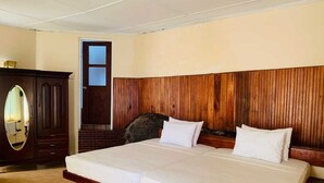 Un grand lit avec une tête de lit en bois, une armoire en bois foncé et une petite fenêtre.