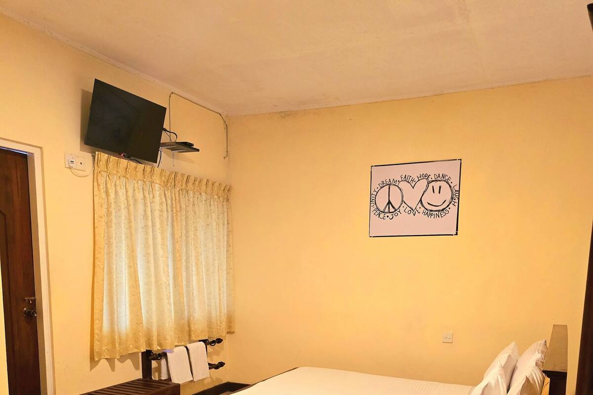 Habitación de hotel con cama, banca, escritorio, televisor y un cartel motivacional en la pared.