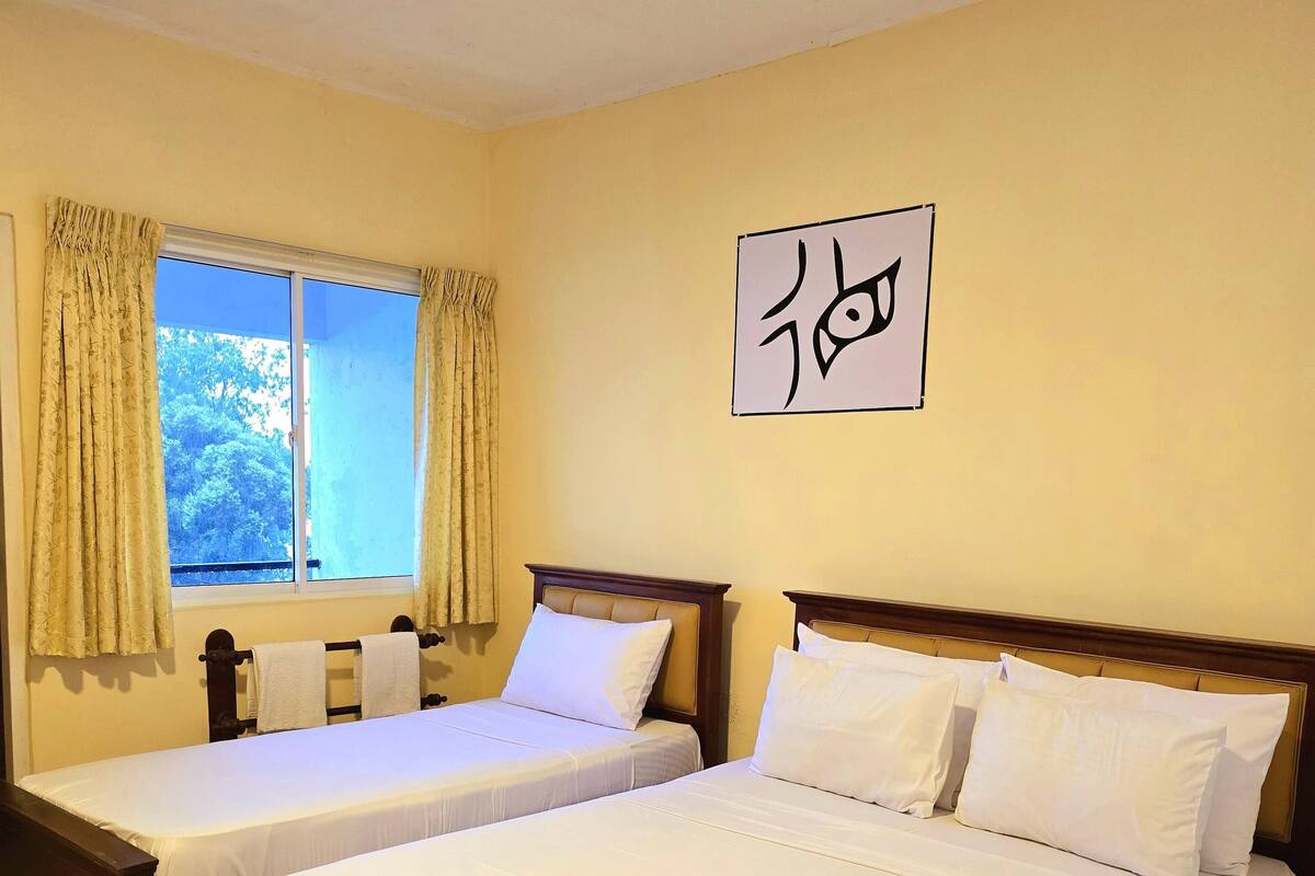 Una habitación de hotel con dos camas individuales, una ventana con cortinas y una pared con un símbolo enmarcado.