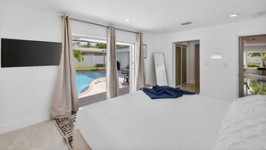 Ein Schlafzimmer mit einem großen Bett, einem an der Wand befestigten Fernseher und Blick auf einen Swimmingpool durch Glastüren.