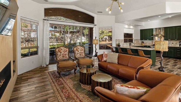 A spacious living room with a large sofa, armchairs, and a coffee table. There is a kitchen area with green cabinets and a dining area with a table and chairs. - Myrinn| Yard w/ Hot Tub, Fire Pit & Red Rock Views (Sedona)