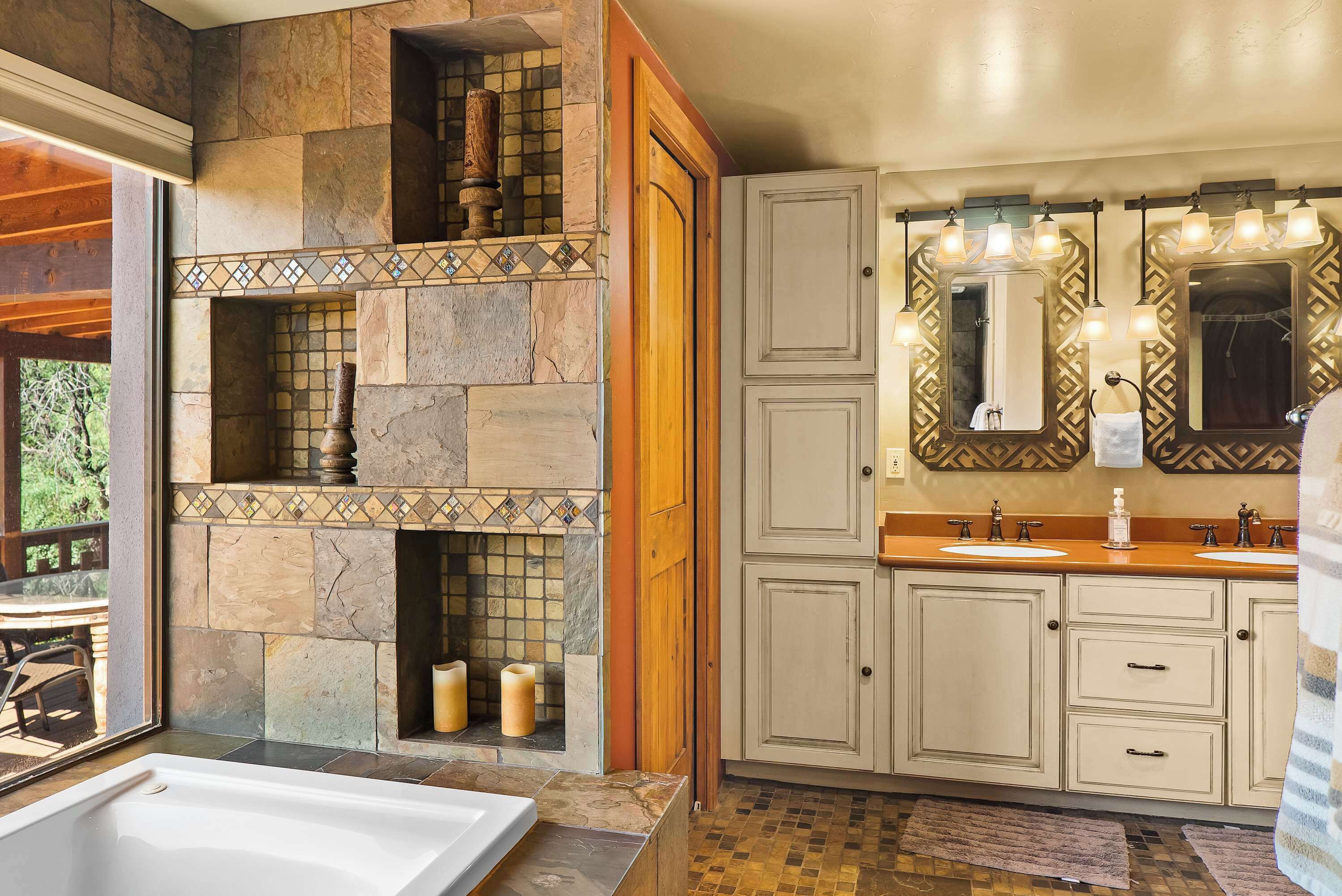 A bathroom with a stone wall, a bathtub, and a vanity with two sinks and a mirror.