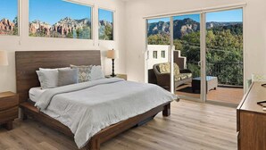 A bedroom with a large bed, a nightstand, a chair, and a balcony with a view of mountains. - Myrinn-360° Red Rock Views, Balcony & Creek Access (Sedona)