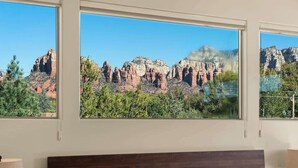 A bedroom with a large window offering a view of red rock formations and greenery. - Myrinn-360° Red Rock Views, Balcony & Creek Access (Sedona)