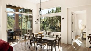 A dining area with a large table and chairs, a chandelier, and large windows offering a view of trees and mountains. - Myrinn-360° Red Rock Views, Balcony & Creek Access (Sedona)