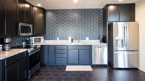 A modern kitchen with dark cabinets, a stainless steel refrigerator, a microwave, and a coffee maker. - Myrinn – Red Rock Views | Hot Tub, Gym & Billiards (Sedona)