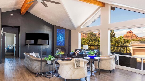 A spacious living area with a high ceiling, modern furniture, and large windows offering a view of a mountainous landscape. - Myrinn – Red Rock Views | Hot Tub, Gym & Billiards (Sedona)