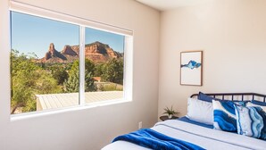 A bedroom with a large window, a bed with blue bedding, and a framed picture on the wall. - Myrinn – Red Rock Views | Hot Tub, Gym & Billiards (Sedona)