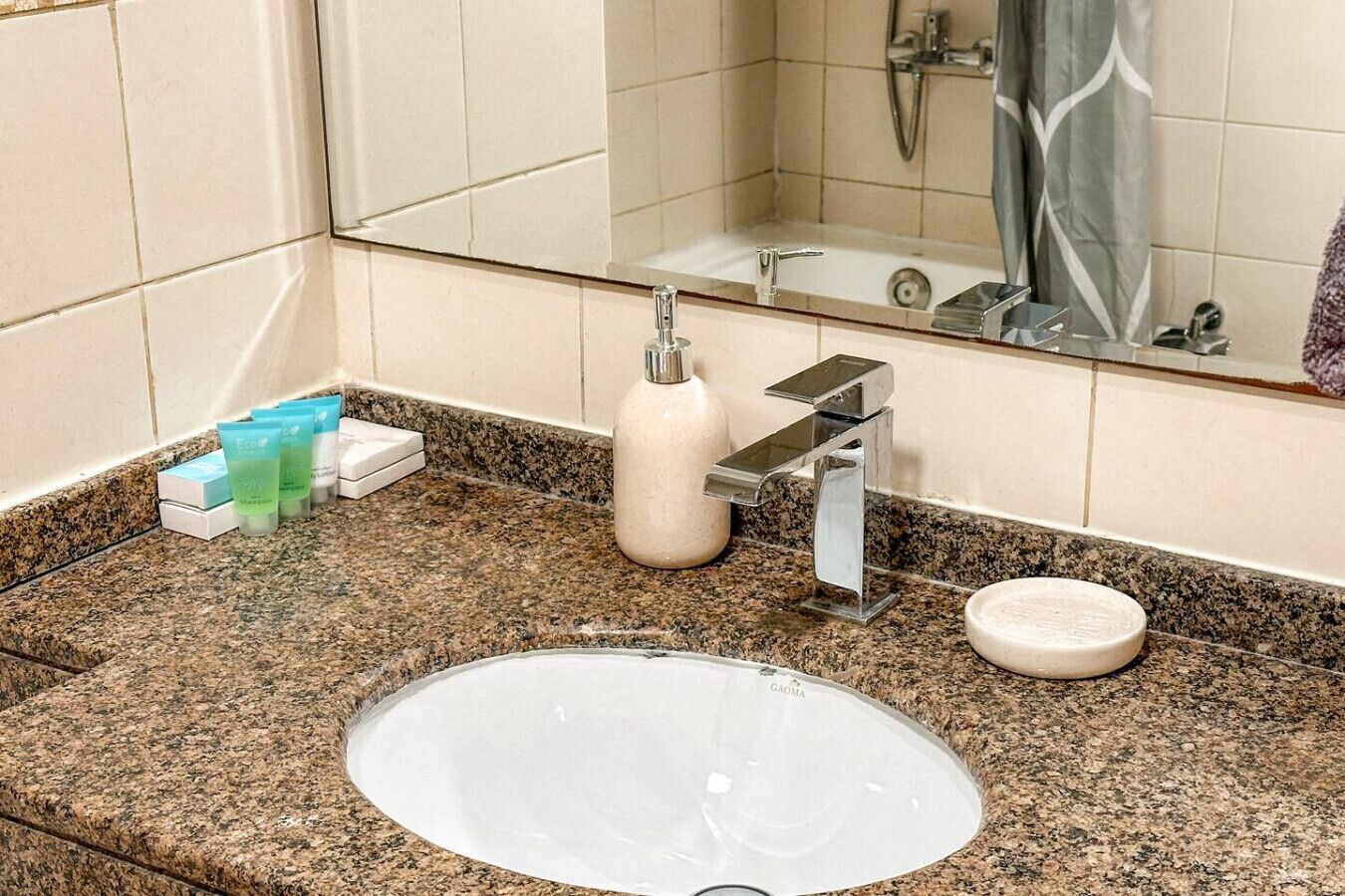 Un baño con encimera de granito, un lavabo, un espejo, una ducha y artículos de aseo.