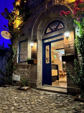 Ein Steinhaus mit einer blauen Tür, einem Schild mit der Aufschrift "MIRNA KOÇUKOY" und einer steilen Steintreppe zum Eingang.