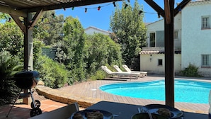 Un espace aménagé au bord de la piscine, comprenant un barbecue, des chaises longues et une table avec des assiettes et des bols.