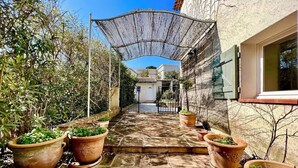 Une cour avec un chemin dallé, des plantes en pot, une pergola et un bâtiment doté d’une fenêtre.